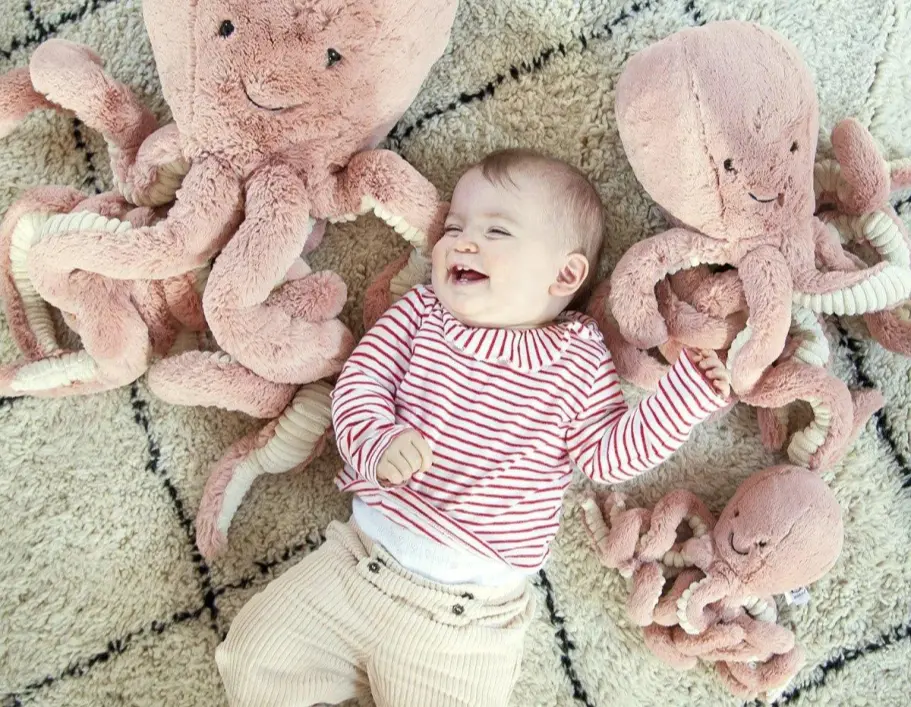 Un bambino sorridente sul pavimento tra vari polpi di peluche rosa